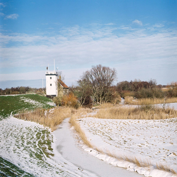 Foto van een besneeuwde Hylperdyk en de vuurtoren